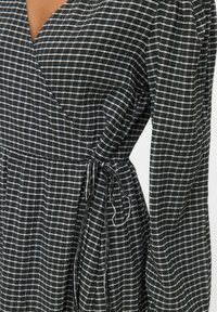 Vestido envolvente a cuadros en blanco y negro con mangas largas atado en un lazo en la cintura, en una persona.