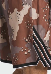 Brune shorts med camouflagemønster lavet af glat syntetisk materiale, med sorte kanter og hvide striber langs sidesømmen.