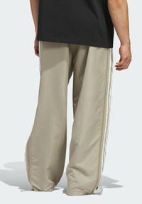 Svijetlosmeđi dukserice s opuštenim krojem, koji imaju uspravne bijele pruge uz bočne šavove i glatku, lagano teksturiranu tkaninu.