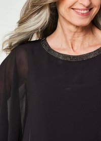 Schwarzes Chiffon-Top mit einem runden Halsausschnitt, der mit einer strukturierten, mit Perlen verzierten Akzentuierung geschmückt ist. Durchsichtige Ärmel betonen das leichte Design.