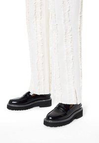 Czarne lakierowane mokasyny na grubej podeszwie, z przeszyciami i gładkim wykończeniem. Zestawione z białymi, fakturowanymi spodniami.