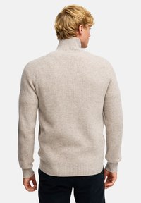 Beżowy sweter z prążkowanego dzianiny z wysokim kołnierzem i dopasowanymi mankietami. Wykonany z miękkiego materiału, charakteryzuje się czystym wykończeniem i minimalnym zdobieniem.