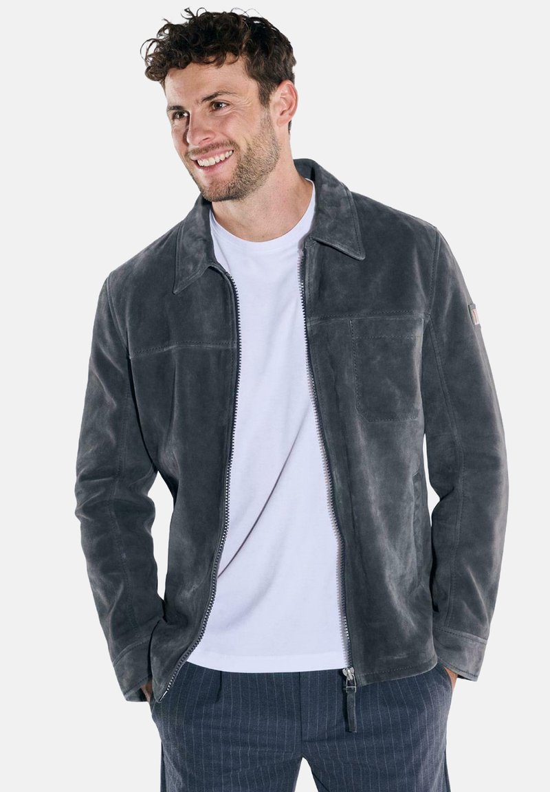 Graue Lederjacke mit Reißverschluss vorne, breitem Kragen und einer Brusttasche. Glatte Textur mit dezentem Glanz, getragen über einem weißen Hemd.