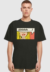 Zwart katoenen T-shirt met een grafische print van de lippen van een vrouw met rode lippenstift en lang blond haar, naast een spraakknop met de tekst "Sjah...!"