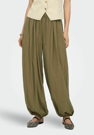 Pantalon ample vert olive avec poignets élastiques froncés, porté avec un haut beige sans manches et des chaussures plates à motifs.