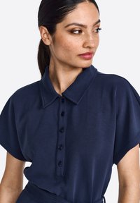 Polo shirt blu navy con colletto e maniche corte, dotato di una chiusura frontale con bottoni e una texture liscia e morbida.