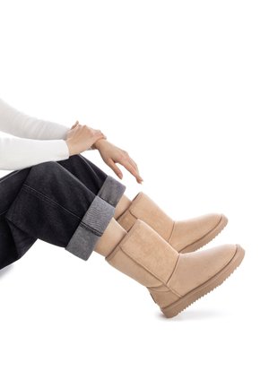 Botas de tobillo de ante beige con punta redonda y paneles laterales texturizados, combinadas con pantalones de mezclilla oscuros doblados en los dobladillos.