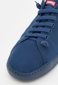 Sneaker blu navy realizzato in tessuto liscio con punta arrotondata, dotato di lacci piatti e dettagli di cucitura in vista, contrassegnato da un'etichetta rossa.