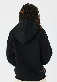 Sudadera negra con una gran capucha, puños y dobladillo acanalados. Presenta un detalle de logo texturizado en la parte posterior. Fabricada con una tela suave.