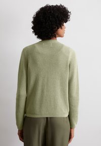 Das handgestrickte Sweatshirt in hellem Grün hat ein strukturiertes Muster, einen Rundhalsausschnitt, lange Ärmel und gerippte Bündchen. Knopfdetail am hinteren Kragen.