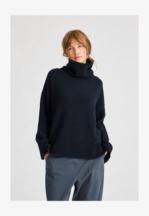 Tamsiai mėlynas golfas, pagamintas iš minkštos mezginio medžiagos. Savybės: raukšlėtas apykaklė ir hem, laisvas kirpimas ir numesti petys.