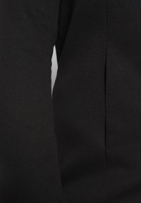 Melna garuma piedurkņu drēbe, kas izgatavota no gludas adītas auduma. Tam ir pieguļošs siluets ar sānu izgriezumu, kas nodrošina brīvību kustībai. Minimālistisks dizains.