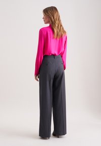 Fuchsia zijden blouse met knoopmanchetten, gecombineerd met charcoal grijze broek met wijde pijpen, voorzien van zijzakken en subtiele streepjes.