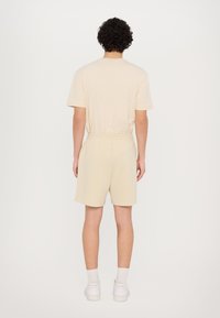 T-shirt en coton beige et shorts assortis, coupe décontractée avec taille élastique, design simple et texture lisse. Pas de motifs visibles.