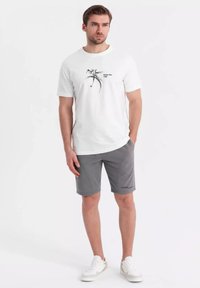 T-shirt blanc avec un graphique de vélo noir et du texte. Associé à un short gris et des baskets blanches, mettant en avant un look décontracté.