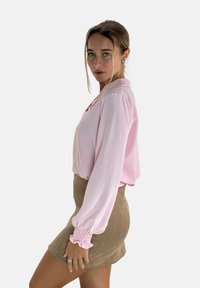 Lichtroze blouse met lange mouwen en een kraag, voorzien van gerimpelde manchetten, gecombineerd met een tan suède minirok met een gladde textuur.
