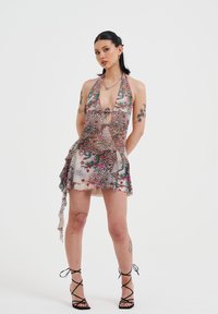 Vestido con cuello halter que presenta un diseño de patrones mixtos con estampados de animales y colores vibrantes; tejido ligero con un dobladillo en capas y detalle de lazo lateral.