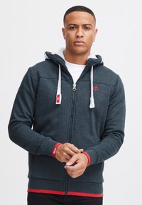 Dunkelgrauer Zip-Hoodie mit weißen Kordeln und roten Akzenten an den Bündchen und am Saum. Verfügt über ein weiches Innenfutter und ein Logodetail.