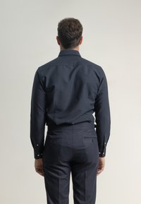 Camisa de botón azul marino con mangas largas y ajuste entallado, combinada con pantalones oscuros a juego. Tejido suave y diseño minimalista.