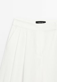 Hvide plisserede bukser med sidelommer og en bred talje. Stoffet har en glat tekstur. Tags viser "Massimo Dutti" branding.