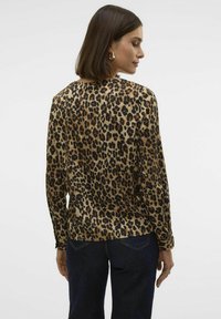 Blusa a maniche lunghe con stampa leopardata in tonalità marroni, caratterizzata da una texture liscia e una vestibilità comoda, abbinata a jeans in denim scuro.