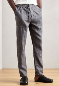Gray linen trousers with a relaxed fit, elastic waistband, adjustable drawstring, and two side pockets. Styled with black clogs.
