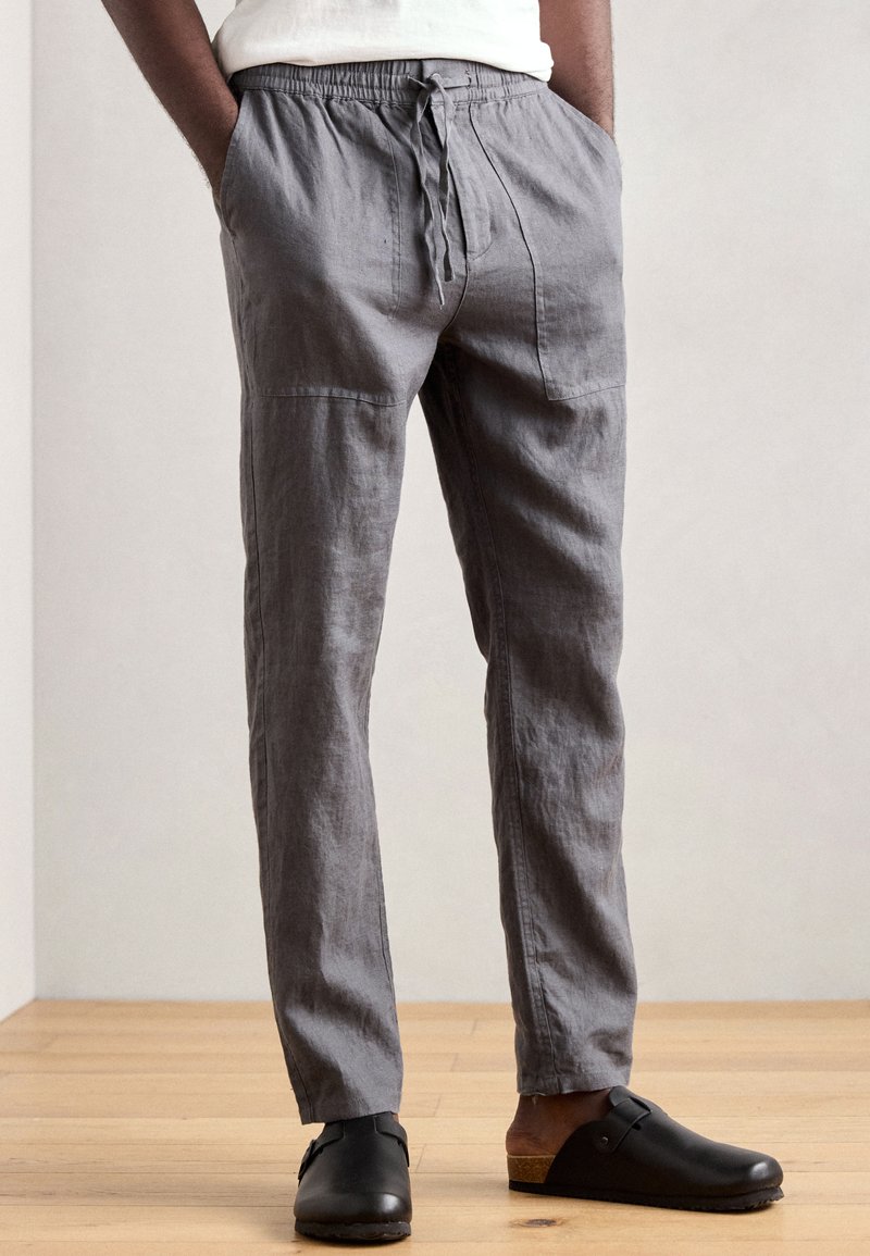 Gray linen trousers with a relaxed fit, elastic waistband, adjustable drawstring, and two side pockets. Styled with black clogs.