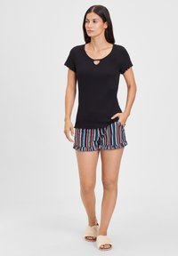 Black short-sleeve top with a keyhole detail paired with striped shorts that have a ruffled hem. Worn with light-colored slide sandals.