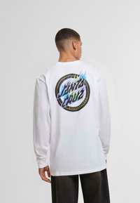 Bílá dlouhá pánská tričko s dlouhým rukávem se barevným grafickým designem na zádech, který obsahuje kruhové logo a stylizovaný text. Měkký bavlněný materiál.
