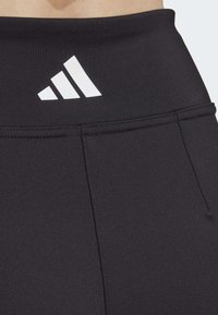 Sorte atletiske leggings med høj talje, der har et hvidt Adidas-logo på fronten og diskrete stikningsdetaljer.
