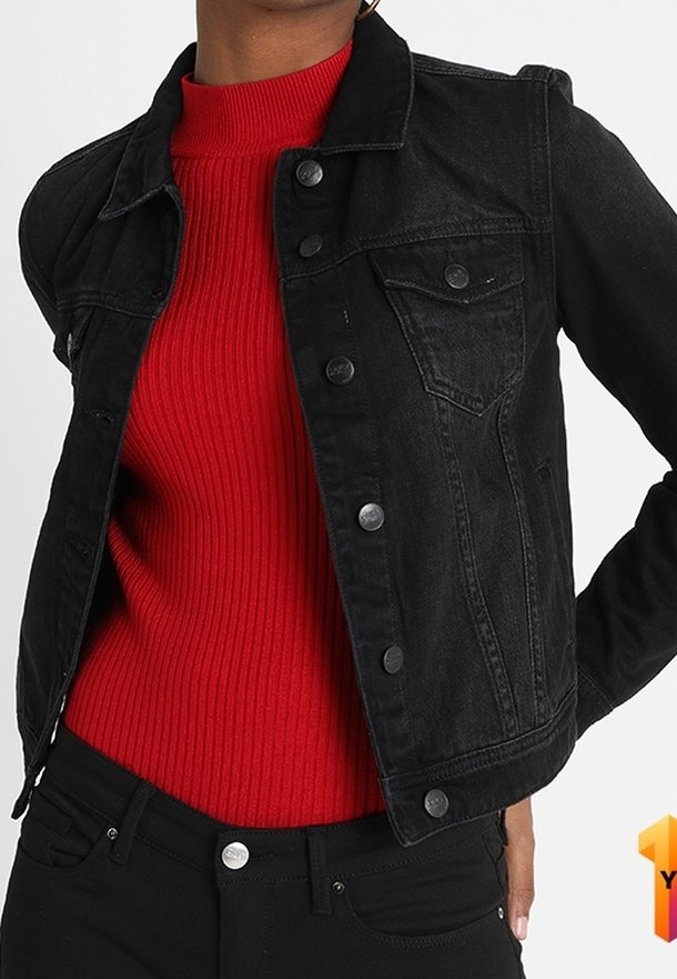 Personne portant une veste en jean noire ajustée sur un pull à col roulé rouge côtelé, associée à un pantalon noir, main reposant sur la hanche.