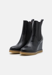 Bottines à wedge en cuir noir avec des panneaux élastiques sur les côtés et une semelle en caoutchouc texturé couleur tan. Fini brillant avec une silhouette épurée.