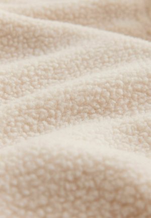 Soft, beige fleece fabric drapes in gentle waves, showcasing its texture and warmth, ideal for blankets or cozy clothing.