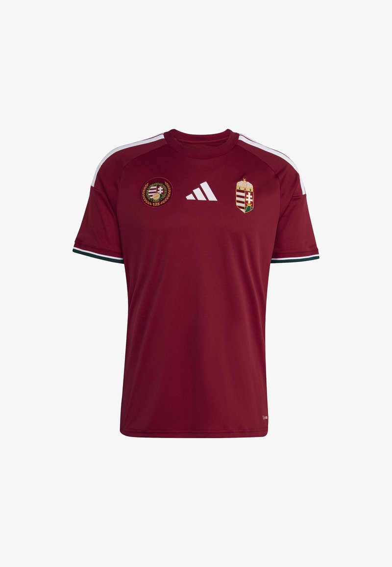 Maglia da calcio di colore marrone realizzata in tessuto sintetico. Presenta strisce bianche sulle spalle, loghi della squadra sul petto e dettagli verdi sulle maniche.