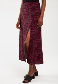 Red and black patterned maxi skirt featuring a high slit, made from lightweight fabric with a heart-shaped print, paired with black block-heeled sandals.