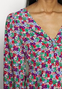 Kwiecista sukienka z dekoltem w kształcie litery V, w mieszance kolorów czerwonego, fioletowego, zielonego i niebieskiego na jasnym tle. Miękka tkanina z marszczonym detalem.