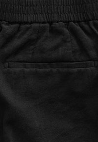 Ceinture élastique noire avec tissu froncé au-dessus d'une poche arrière plate sur un pantalon ou un short décontracté.
