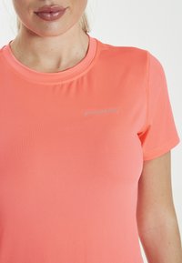 Pink athletic shirt in a smooth, stretchy fabric with short sleeves. Features a round neckline and a small, gray "ENDURANCE" logo on the chest.