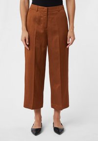 Pantalons larges taille haute marron en tissu doux, avec des plis avant et un ourlet propre. Associés à des chaussures noires à bout pointu.