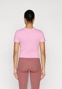 Ροζ κοντομάνικο εφαρμοστό μπλουζάκι που φαίνεται από πίσω, σε συνδυασμό με ροζ κολάν με ψηλή μέση, που αναδεικνύουν λεία υφή και τακτικές ραφές.