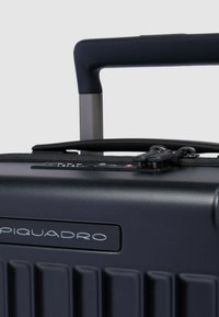 Hartschalenkoffer in Marineblau mit strukturierter Oberfläche und vertikalen Rillen, ausziehbarem Griff und Reißverschluss mit Metallakzenten.