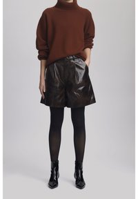 Brown knit turtleneck sweater, high-waisted dark leather shorts, paired with black sheer tights and shiny ankle boots.