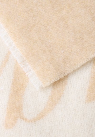 Tejido de lana suave beige y blanco con un borde doblado que muestra una superficie texturizada y esponjosa y un sutil patrón marrón claro.