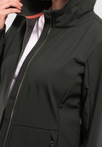 Zielona kurtka typu softshell z wysokim kołnierzem, przednim zamkiem błyskawicznym i dwoma bocznymi kieszeniami. Posiada kontrastowe pomarańczowe akcenty na wewnętrznej stronie kołnierza.