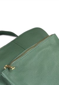 Groene leren tas met textuur en een gedeeltelijk open gouden rits, die de handgreep en de gedetailleerde stiksels toont.