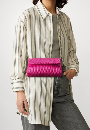 Personne portant une chemise rayée beige et un pantalon gris avec un sac bandoulière rose vif texturé accroché au niveau de la taille.
