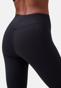 Zwarte leggings van rekbaar materiaal, met een hoge tailleband en een gladde textuur. Het ontwerp heeft minimale naden voor een gestroomlijnde pasvorm.