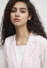 Witte blazer met verticale strepen in roze en bruin, gemaakt van een lichtgewicht stof. Met inkepingen aan de revers en een getextureerde afwerking. Eenvoudig wit onderhemd.