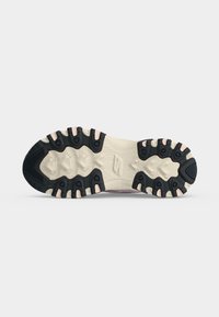 Semelle d'une chaussure de randonnée avec une bande de roulement noire et beige, conçue pour la traction sur un terrain accidenté, présentée sur un fond clair uni.