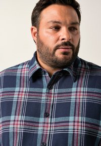Camicia a quadri blu navy realizzata in tessuto morbido, con righe verdi, rosse e bianche, chiusura con bottoni e colletto a punta.
